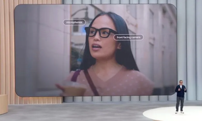 Large screen shows woman wearing glasses with integrated microphones and camera; presenter stands below.