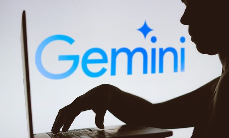 Silhouette of a person using a laptop displaying the bright blue Google Gemini logo.
