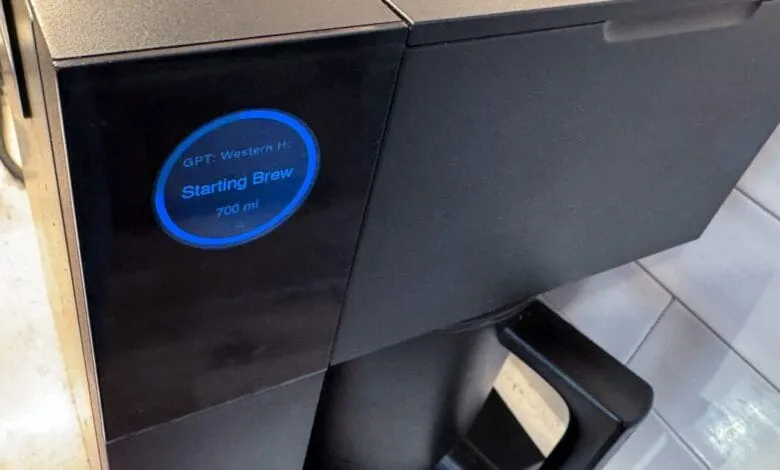 Close-up of a black coffee machine displaying 'Starting Brew 700 ml' on a blue circular indicator.