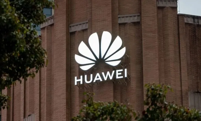 Illuminated Huawei logo on a brick building at night, partially obscured by trees.