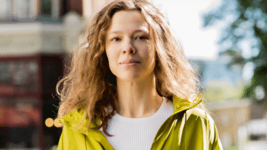 Woman, stealth AI model, with long curly hair wearing a yellow jacket, standing outdoors in a city setting.