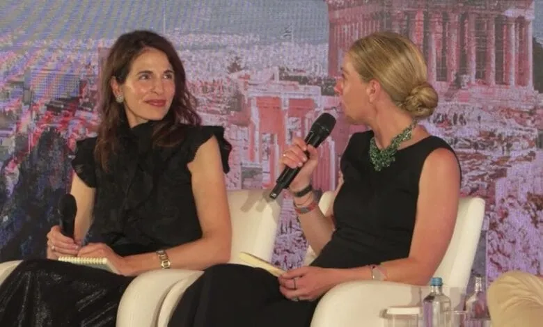 Two women in black dresses participate in a panel discussion against a backdrop of ancient Greek ruins.