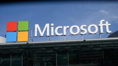 Microsoft logo and name on a modern glass building against a bright blue sky.