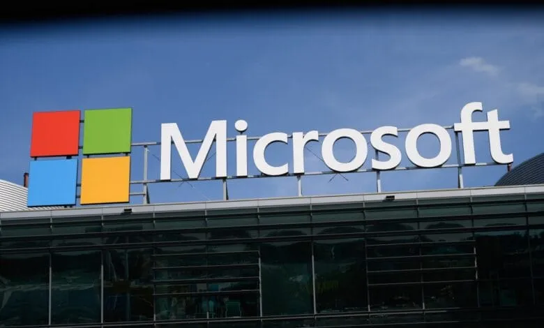 Microsoft logo and name on a modern glass building against a bright blue sky.