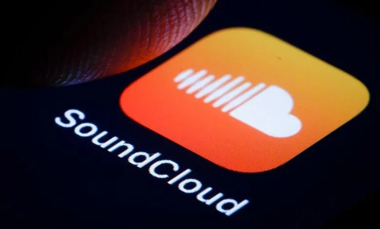 Close-up of a finger about to tap the SoundCloud app icon on a smartphone. The icon is orange and white.
