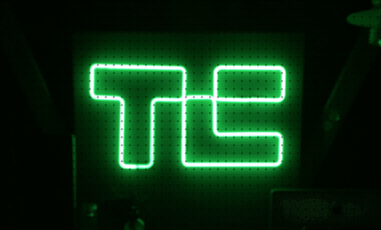Bright green neon 'TE' sign on a dark green wall with a subtle grid pattern.