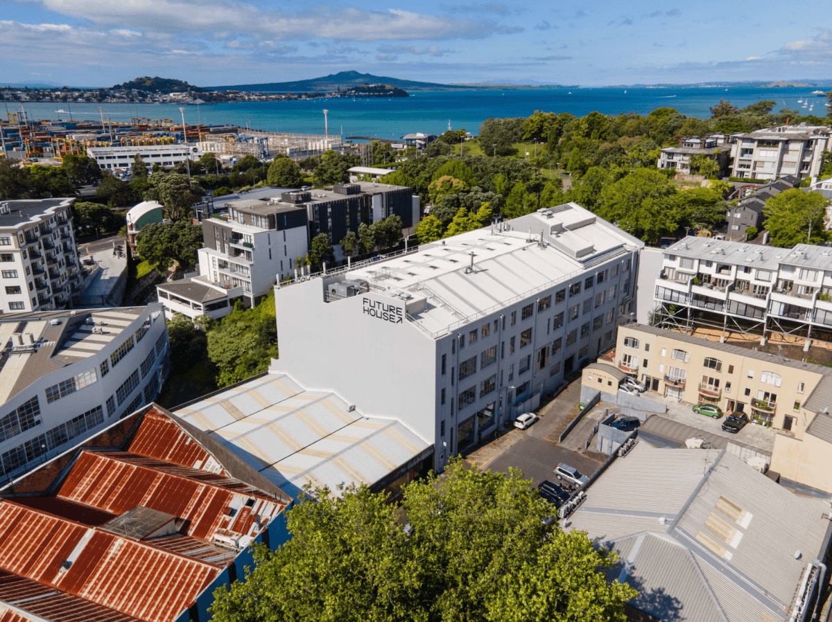 Aerial view of Future Houses building in Auckland, New Zealand, with harbor and city in background.