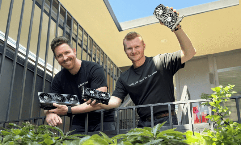 Two men stand on a balcony, holding several high-end graphics cards. One shirt says 'LLMs will never be the same'.