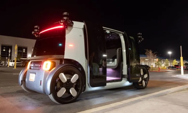 A futuristic, self-driving Zoox vehicle at night, doors open, showing its interior. Sensors are visible on the roof.