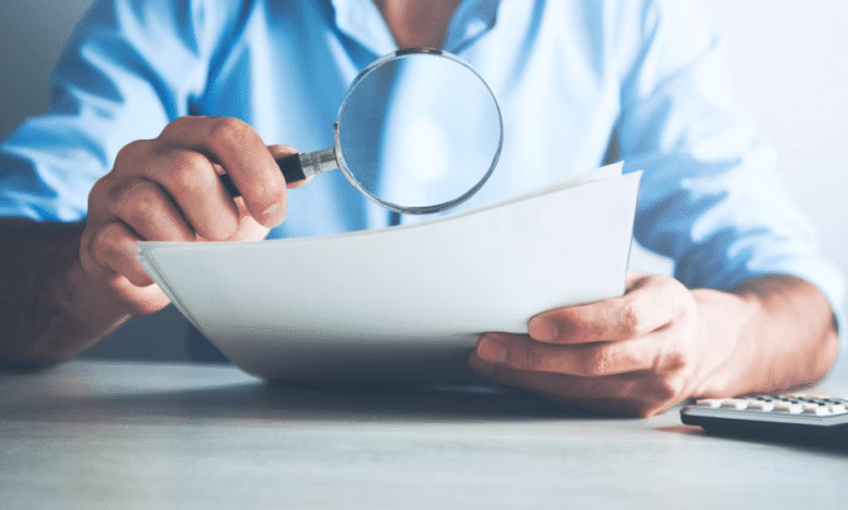 Close-up of hands holding documents and a magnifying glass, reviewing details carefully.