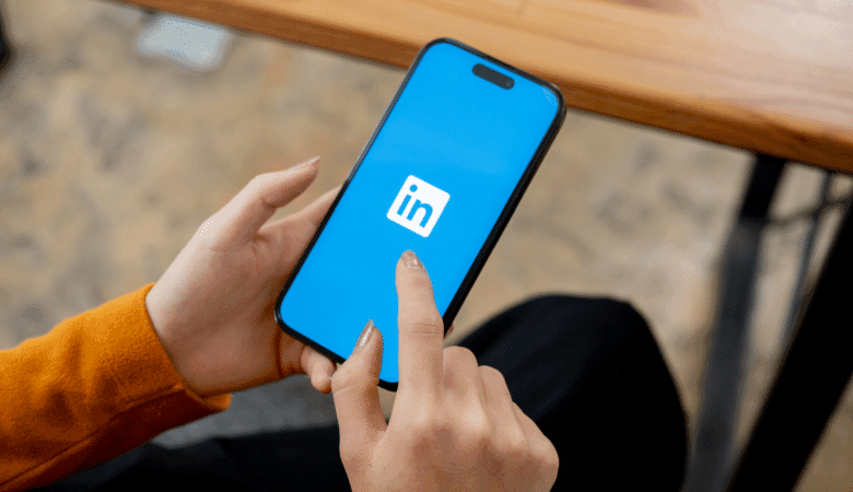 Close-up of hands holding a smartphone displaying the LinkedIn logo on a bright blue screen.