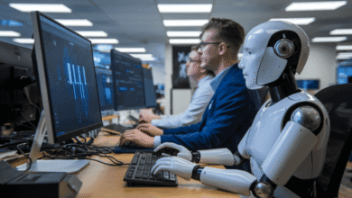 A robot and two humans work side-by-side at computers, analyzing data displayed on screens.