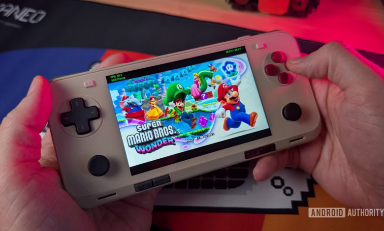 Hands hold a beige AYANEO Pocket ACE handheld gaming device playing Super Mario Bros. Wonder. The screen shows Mario and Luigi in a vibrant level.
