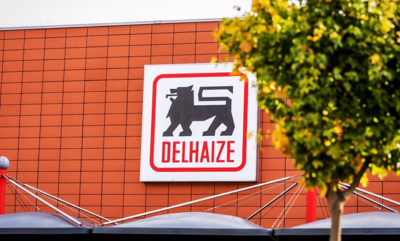 Delhaize supermarket logo on a terracotta building, partially obscured by a tree.