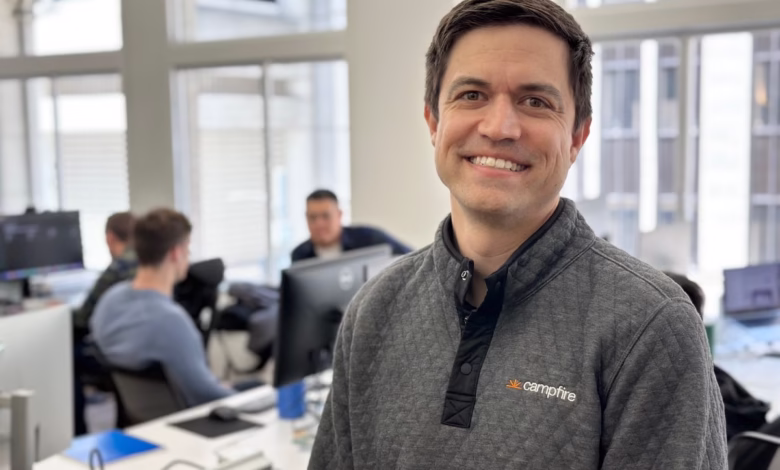 John Glasgow, Campfire CEO, smiles warmly in his office, colleagues blurred in the background.