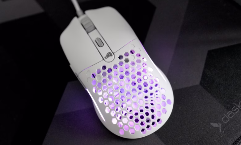 White gaming mouse with honeycomb design and purple LED lighting rests on a black mousepad.