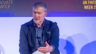 A man in a blue jacket speaks at UK Fintech Week 2023. The background features event branding.