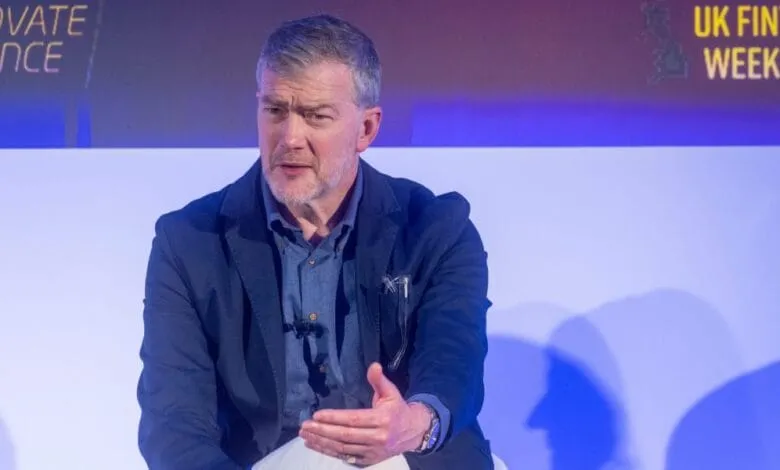 A man in a blue jacket speaks at UK Fintech Week 2023. The background features event branding.