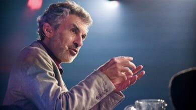 Yoshua Bengio gives a presentation, his hands gesturing animatedly. He's wearing a light gray jacket.