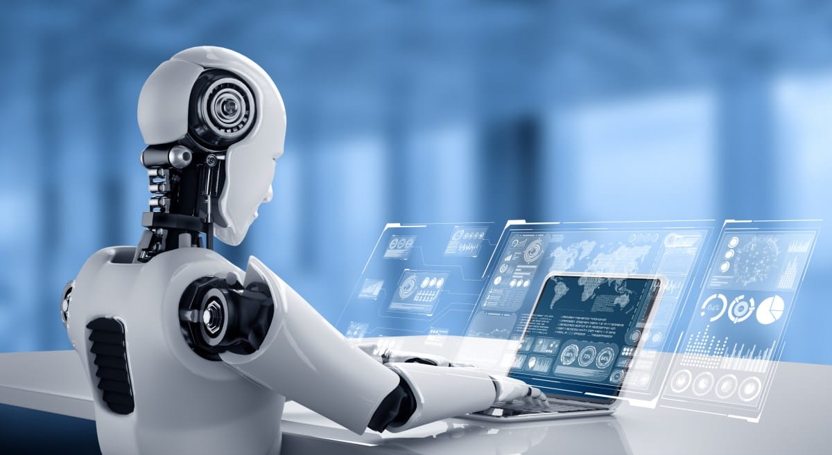 A white robot sits at a desk using a laptop with holographic displays showing data charts and graphs.