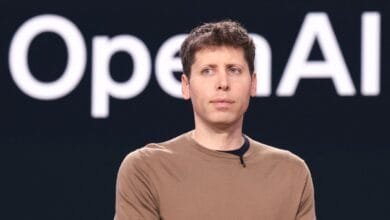 Sam Altman, CEO of OpenAI, stands against a dark background with the OpenAI logo visible.