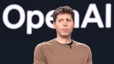 Sam Altman, CEO of OpenAI, stands against a dark background with the OpenAI logo visible.