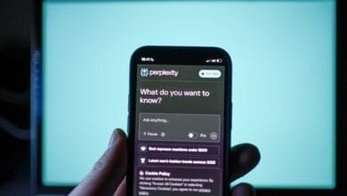 A hand holds a phone displaying the Perplexity AI app, prompting 'What do you want to know?', with search suggestions visible. A teal screen is in the background.