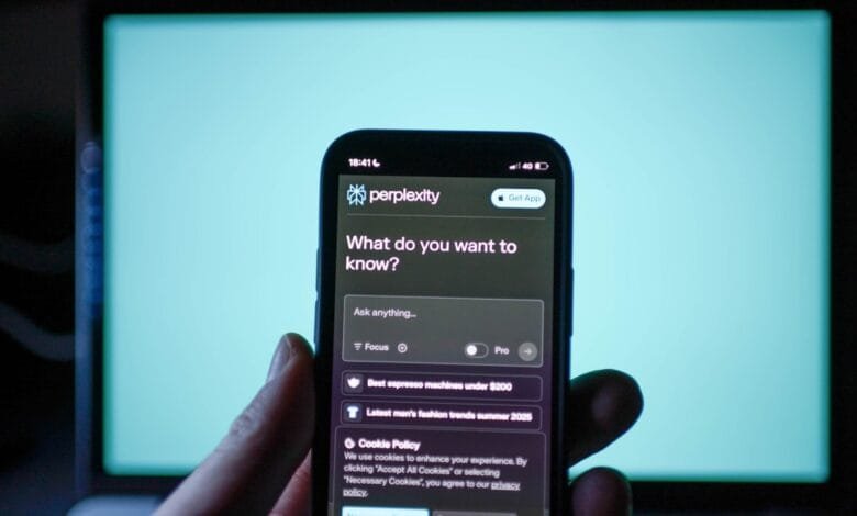 A hand holds a phone displaying the Perplexity AI app, prompting 'What do you want to know?', with search suggestions visible. A teal screen is in the background.