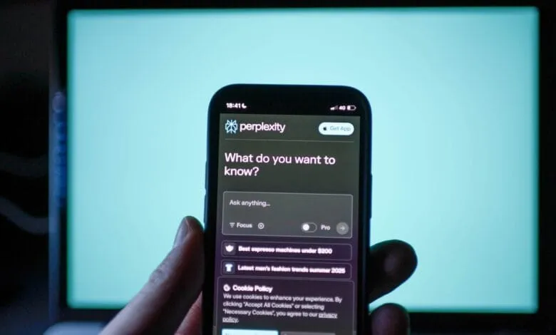 Hand holding phone showing Perplexity AI app's interface, prompting 'What do you want to know?' with search suggestions.