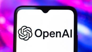 Close-up of a smartphone displaying the OpenAI logo on a white background against a blurred purple and blue backdrop.