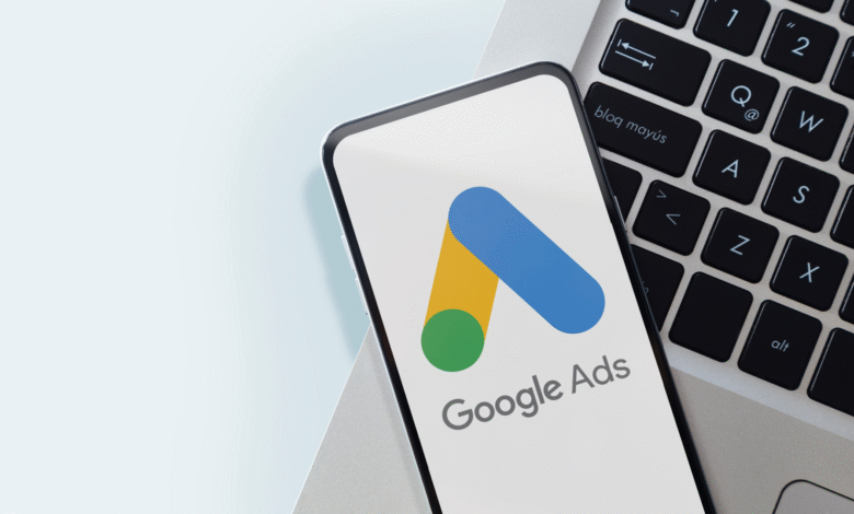 Smartphone displaying the Google Ads logo rests on a laptop keyboard; clean, modern aesthetic.