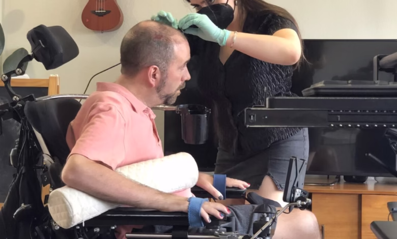 A researcher prepares a person in a wheelchair for a brain-computer interface (BCI) experiment, carefully attaching sensors to their head.