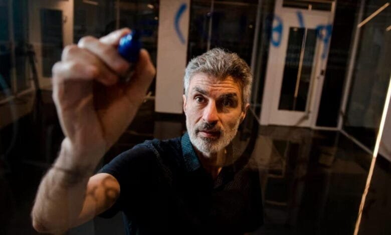 Yoshua Bengio, a renowned computer scientist, writes on a glass wall with a blue marker.