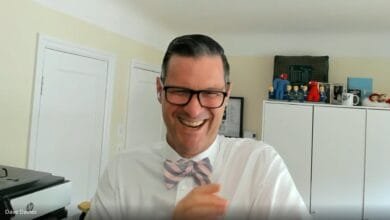 Dave Davies, author and journalist, laughs heartily during a video interview, wearing a pink and grey bow tie.