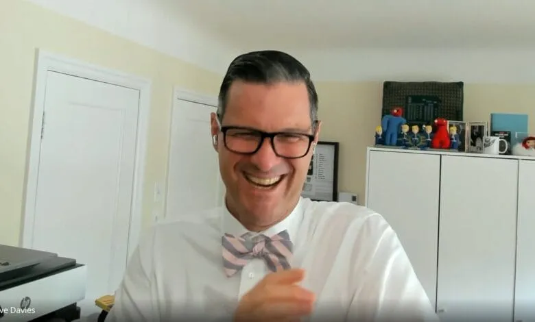 Dave Davies, author and journalist, laughs heartily during a video interview, wearing a pink and grey bow tie.
