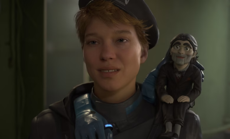 A woman in a dark jacket and beret smiles gently, a ventriloquist's dummy perched on her shoulder.