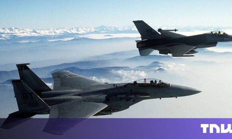 Two fighter jets fly in formation over a mountain range, showcasing their sleek designs against a hazy sky.