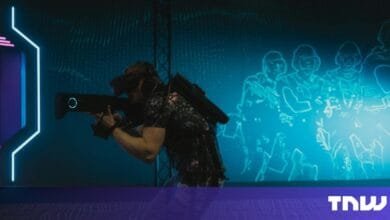Person wearing VR headset and backpack holds futuristic weapon, immersed in a blue, digital battlefield projected on a wall.
