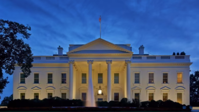 The White House at dusk, illuminated, with a fountain in the foreground.