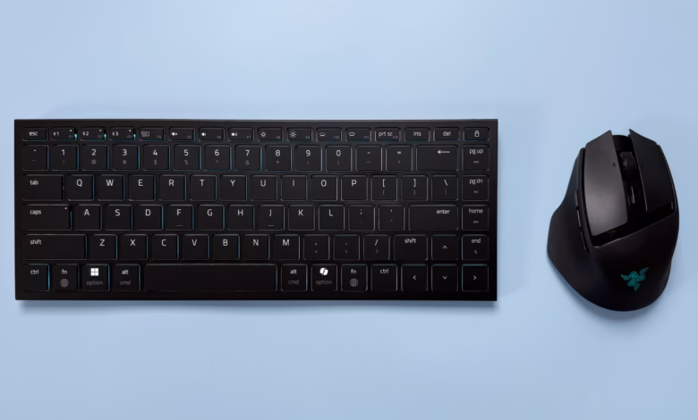 A black keyboard and mouse sit on a light blue surface. The keyboard has teal accents, and the mouse has a Razer logo.
