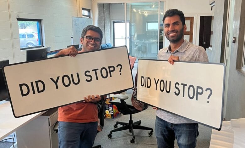 Ali Rehan and Dhruv Maheshwari hold signs that read 'Did you stop?' in a modern office setting.