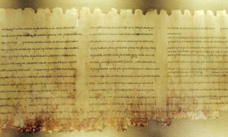 Close-up of an ancient, fragmented parchment scroll displaying faded text in an unknown script.