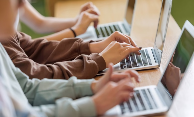 Close-up of students' hands typing on laptops, showcasing collaborative learning.