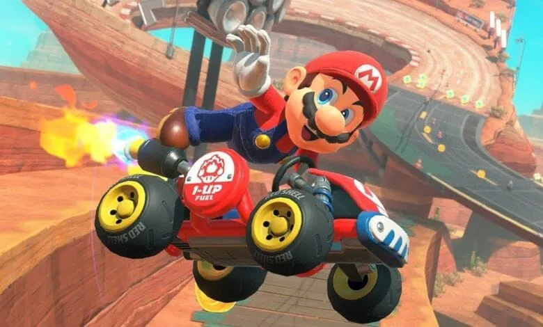 Mario Kart 8 Deluxe: Mario in a red kart with flames, soaring over a desert-like racetrack.