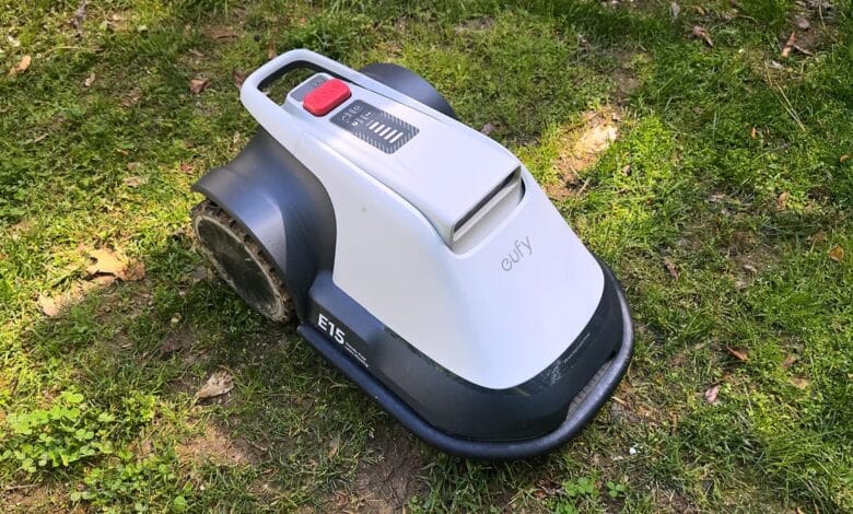 A white and gray robotic lawnmower, the Eufy E15, sits on a patch of grass.