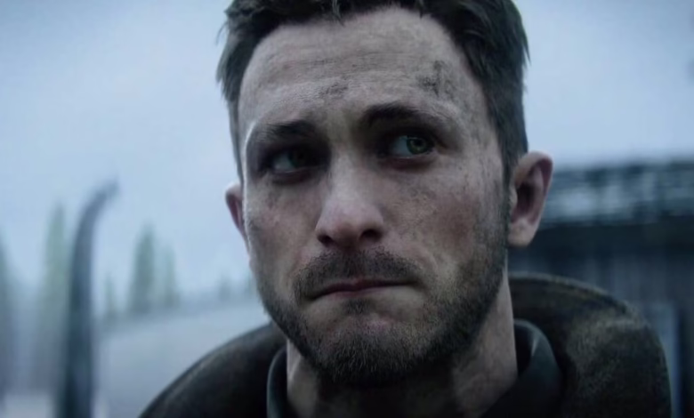 Close-up of a man's weathered face, showing dirt and stubble. He appears serious and pensive, set against a blurred industrial background.