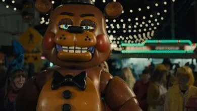 A large animatronic bear, Freddy Fazbear, stands at a nighttime carnival, surrounded by blurry figures in costumes.