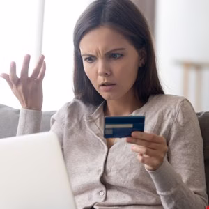 Frustrated woman looks at credit card and laptop, experiencing online payment issues.