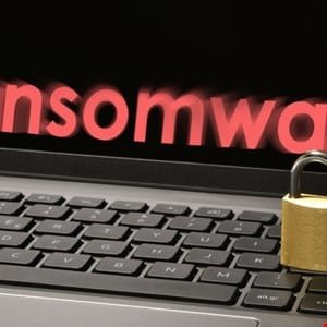 Close-up of a laptop with the word 'ransomware' in red on the screen, and a padlock on the keyboard, illustrating cybersecurity threats.