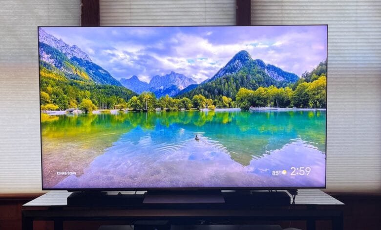 A serene lakeside scene displayed on a large TV screen, reflecting mountains and trees in its tranquil waters.